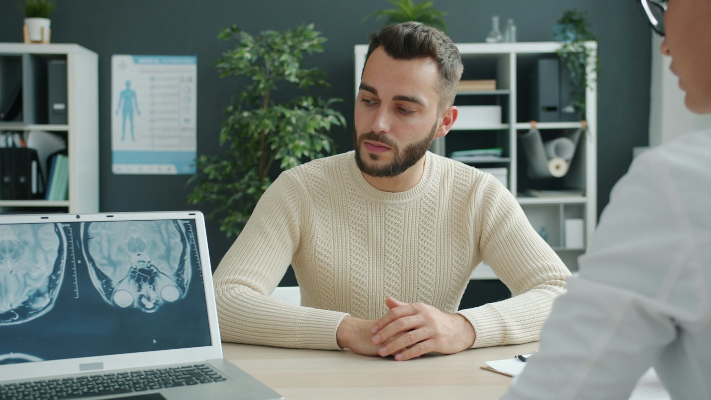 Medico discute i risultati di una TAC cerebrale con un paziente al computer.